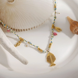 Bohemian beach style necklace with gold fishbone and seahorse charms on a white plate