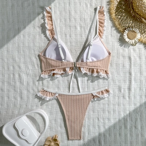 Flat lay of peach ribbed bikini set with white lace trim and summer vacation accessories