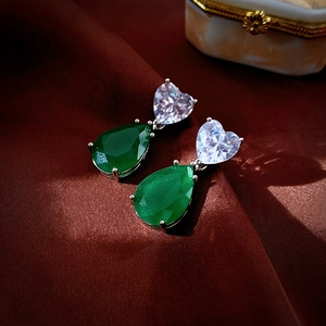 Detail of silver heart and green teardrop zircon earrings on red silk fabric