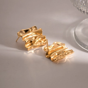 Macro detail of gold-tone rectangular earrings with irregular ripple texture and metallic luster