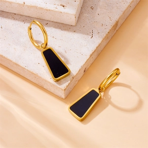 Minimalist gold and black geometric earrings with trapezoid pendants on stone background