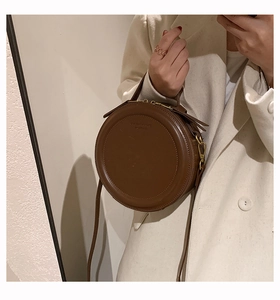 Detailansicht einer runden braunen Vintage-Tasche mit Textprägung und oberem Handgriff
