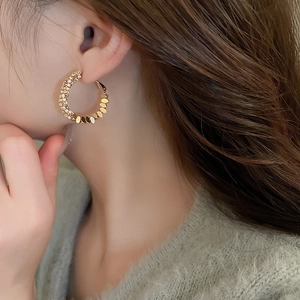 Close-up of C-shaped gold metal hoop earrings with sparkling zircon and oval link detail