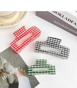 Detailed view of red, black, and green checkered acrylic hair claws on a book