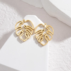 18K gold plated stainless steel monstera leaf stud earrings on a white textured stone base