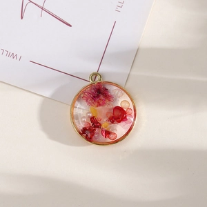 Round golden alloy pendant with red dried flowers and pearls on minimalist background