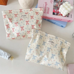 Flat lay of pink and blue bow-printed canvas cosmetic bags with woven labels on a white desk