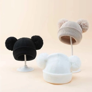 Close-up of knit hats in black, beige, and white with dual fluffy pom-poms on top