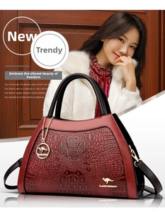 Macro shot of burgundy crocodile texture and golden kangaroo logo on crossbody handbag