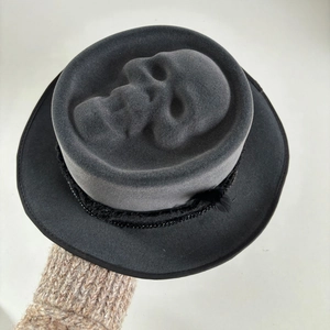 Detailed top view of black felt hat featuring 3D skull relief with chain and feather accents