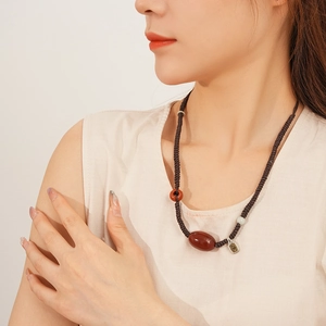 Macro view of woven cord necklace featuring red agate beads and a silver pendant detail