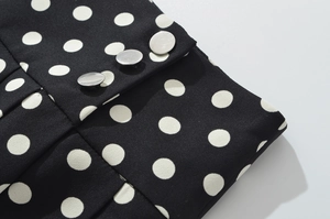 Détail du tissu de jupe à pois noirs avec trois boutons plats argentés et plis