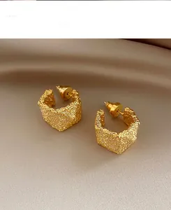 Detailed view of golden C-shaped hoop earrings with lava texture on champagne satin