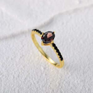 Macro shot of oval red garnet ring with black zircon side stones and gold plated finish