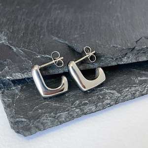 Detailed macro view of square U-shaped silver hoop earrings on a textured black slate