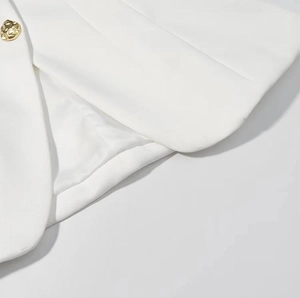 Détail d'un blazer blanc avec col en V, bouton doré texturé et finitions de couture qualité