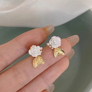 Close-up of white resin rose stud earrings with golden leaves and tiny pearls details