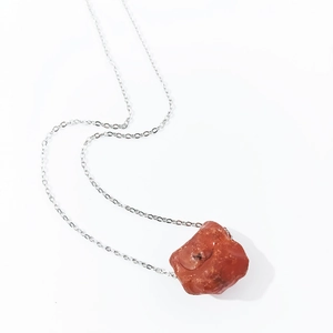 Close-up of raw reddish-brown natural crystal pendant on a fine silver-tone chain