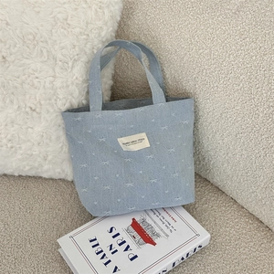 Détail du sac cabas en jean bleu clair avec broderie de nœud blanc et étiquette tissée