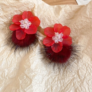Detailed macro view of red acrylic flower earrings with plush pompom on textured paper