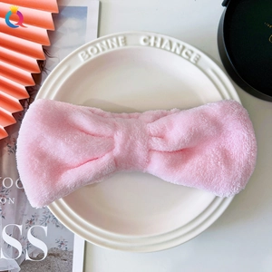 Close-up of soft pink coral fleece headband with a bow knot on a white ceramic plate