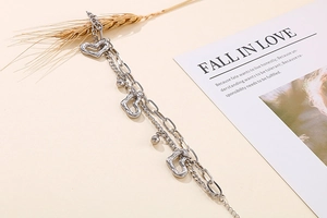 Détail d'un bracelet argenté multicouche avec breloques cœur et perles sur fond chaud