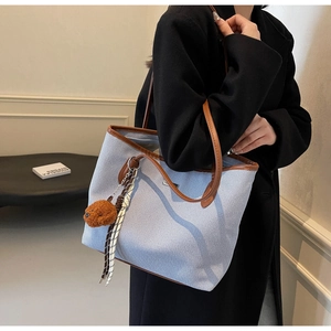 Detail of light blue canvas tote bag featuring brown leather trim and a cute teddy charm