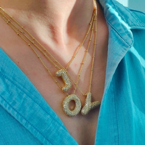 Gros plan des colliers dorés JOY avec pendentifs lettres pavés sur du denim