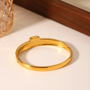 Gold stainless steel bangle with striped texture and zircon inlay on a white surface