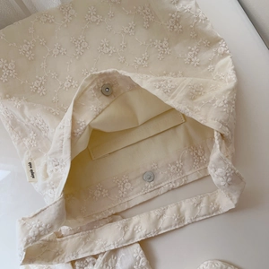 Close-up of cream cotton canvas bag featuring floral embroidery and silver magnetic clasp