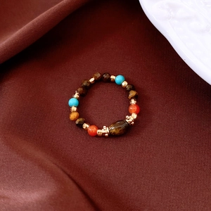 Detailed view of elastic tiger eye bead ring with turquoise accents on brown silk