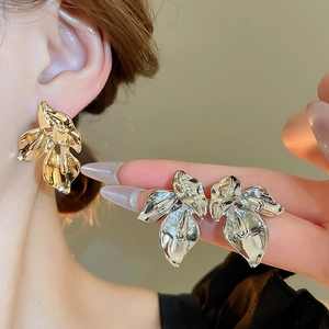 Macro detail of irregular pleated metal flower earrings in polished gold and silver finish