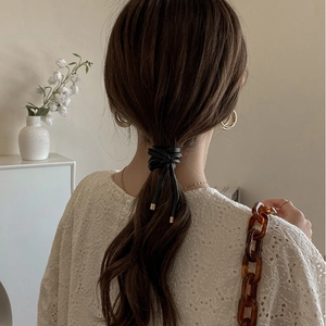 Detail view of a black faux leather wrap hair tie with metal buckles on a low ponytail