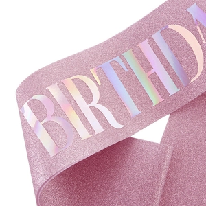Close-up of pink glittery birthday sash featuring holographic reflective lettering detail