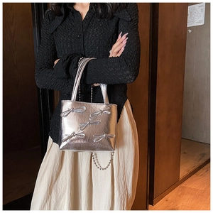 Detail view of a silver square handbag with bow accents and a metal chain strap