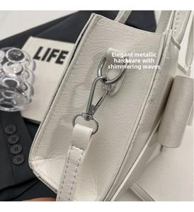 Macro view of polished silver metal hooks and textured white leather on a crossbody bag