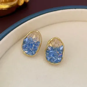 Elegant gold-plated oval earrings with gradient blue crystals on beige leather tray