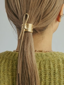 Detail of golden metal knot hair ring with long snake chain tassel on a low ponytail