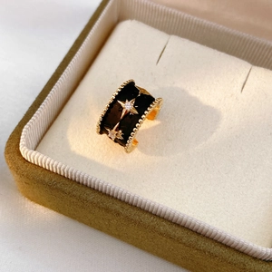 Détail macro d'une bague dorée avec émail noir, motifs étoilés et pierres en zircone