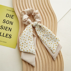 Detail of a beige floral ponytail scarf scrunchie on a decorative wooden tray