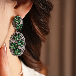 Close-up of vintage oval drop earrings featuring green gems and pave white crystals