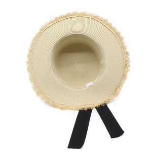Detailed top view of raffia sun hat with raw tassel edges and a black ribbon tie