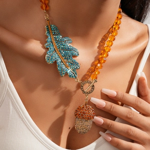 Detail of crystal leaf and acorn pendant with amber beaded chain on a white top