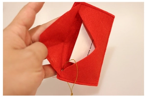 Macro detail of red felt Christmas tree envelope ornament with golden hanging string