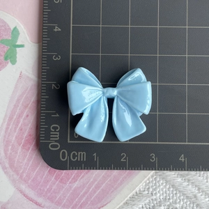 Close-up of light blue resin bow charm showing dimensions 3.5cm x 3cm on a scale mat