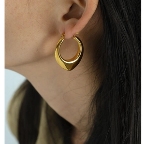 Close-up of golden U-shaped hollow earrings with smooth metallic finish on a model