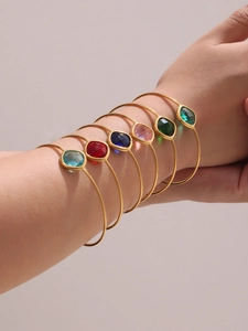 Close-up of seven stackable gold-plated stainless steel bangles with colorful gemstones