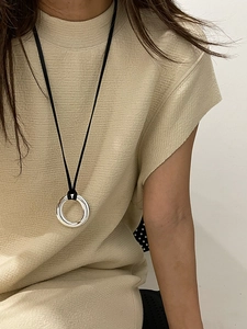 Close-up of a silver circular pendant on a black cord necklace worn with a beige sweater