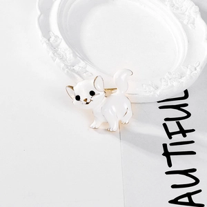 Close-up of white cat brooch with gold trim and black eyes on a minimalist tray