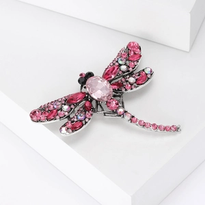 Detailed view of silver dragonfly brooch featuring pink crystals on white display